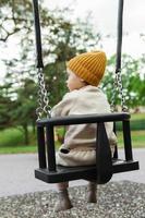 Cute baby boy sitting on a swing in public park photo