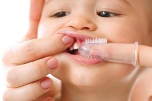 madre cepillando suavemente sus pequeños dientes de niño. foto