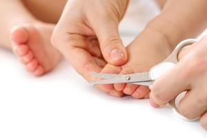 Mother holding little child's foot and cutting toenails. photo