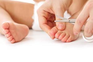 Mother holding little child's foot and cutting toenails. photo