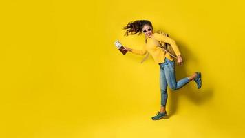 Woman traveler with suitcase, holding passport with ticket on Yellow background. Portrait of smiling happy girl in the yellow dress. people traveler photo