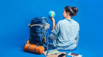 vacaciones de planificación turística con la ayuda del mapa del mundo con otros accesorios de viaje alrededor. viajero mujer con maleta sobre fondo de color azul. chica con una bola de globo en la mano. mochila de viaje foto