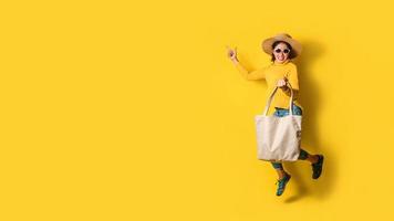 retrato de una hermosa niña emocionada con vestido y gafas de sol con bolsas de la compra. alegre joven con bolso sobre fondo amarillo. moda de compras adicta a las compras. foto