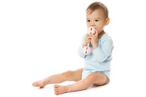 niño pequeño en mameluco sentado y jugando con sonajero de plástico. foto