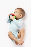 Little boy in romper lying and playing with plastic toy. photo