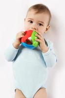 Little boy in romper lying and playing with plastic toy. photo