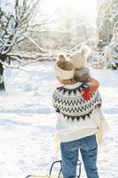 Young mother and her cute little son with retro sled in a snowy park during sunny day photo