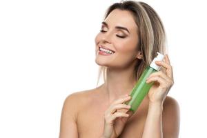 mujer joven con una piel suave sosteniendo una botella de gel limpiador verde foto