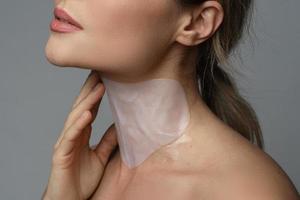 Woman with a moisturizing and anti aging sheet mask applied on her neck photo