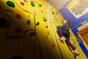 Little girl climbing a rock wall indoor. Concept of sport life. photo