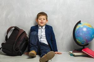 Happy cute clever boy in glasses with school bag and book. Modern backpack. Child is ready to answeron a background. First time to school. Back to school photo