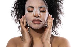 Beautiful black woman with a smooth skin applying facial sheet mask photo