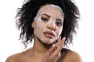 Beautiful black woman with a smooth skin applying facial sheet mask photo