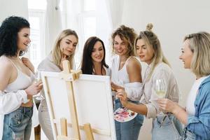 Group of women paint on canvas and drinking white wine during party at home photo