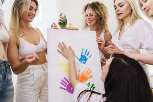 Group of women paint on canvas and drinking white wine during party at home photo