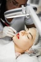 Permanent makeup artist and her client during lip blushing procedure photo