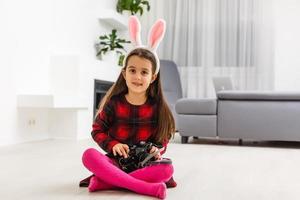 Surprised little girl wearing bunny ears, lying on light wooden floor on Easter Holiday. photo