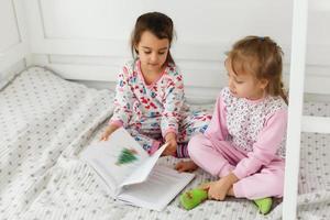 two little smiling lovely sisters in white bed, top, view photo