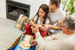 familia sonriente con abuelos sosteniendo un álbum de fotos en casa