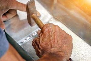 Closeup hands of laborer holding small hammer hit on aluminum lumber and floor tiles at construction site with sun flare background. photo