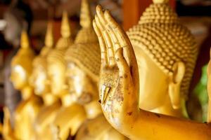 Closeup and crop hand of golden Buddha statue with a gold leaf on blurred golden Buddha statue stand strong line background photo