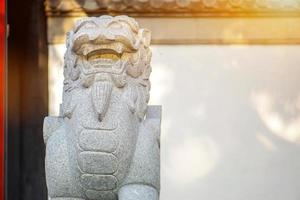 Closeup and crop Chinese lion figurine, stone sculpture in front of Chinese shrine wall with sun flare background. photo