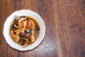 Top view Chinese vegetarian food Tofu and dry vegetables stewed in the gravy on white ceramic bowl and wooden table with copy space for texts background. photo