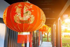 Closeup beautiful Chinese decoration red lanterns hang on ancient shrine ceiling with blurry and sun flare background. Chinese letters on lantern is mean fortune blessing compliment in English. photo