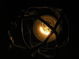 a light bulb glows in an old rusty lamp with a bent metal frame. photo