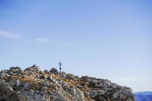 pequeña cruz de cumbre en una montaña rocosa con cielo foto