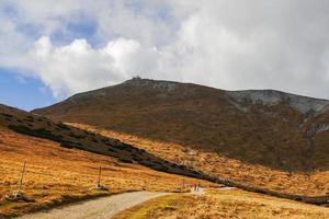 long dirt road through a hilly landscape with view to the summit from the highest mountain photo