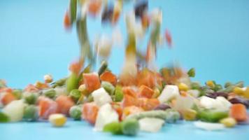 Caída de verduras congeladas surtidas, comida voladora sobre fondo azul. video