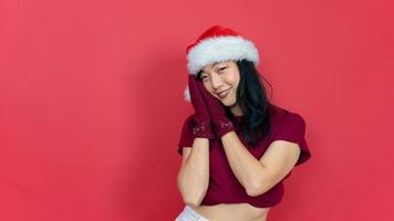 joven mujer hermosa con sombrero de santa de navidad sobre fondo rojo aislado durmiendo cansado soñando y posando con las manos juntas mientras sonríe con los ojos abiertos. foto