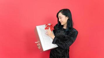 Beautiful Young smiling happy woman wearing evening dress and hold big giftbox over red background. Happy New Year 2023 celebration concept photo