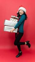 Young asia woman with santa hat and holding Christmas gift isolated red background. Emotion smile. Concept of the New Year and Christmas Day. photo