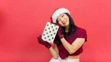 Portrait of a lovely lady dressed in christmas hat holding present boxes at her face isolated over red background photo