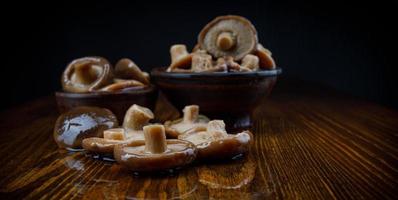 Pickled mushrooms in clay cups stand on a wooden table . Salted mushrooms . Rustic food . photo