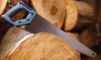 A hand hacksaw with a blue wood handle saws a log. The background is made of wood logs. photo