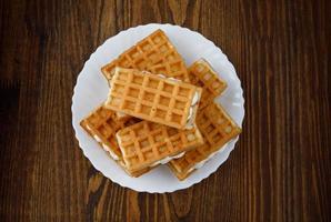 A pile of ruddy Viennese waffles lie on a white plate on a wooden background. photo