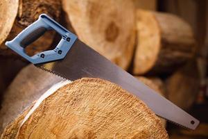 A hand hacksaw on a tree saws a log. The background is made of wood logs. photo