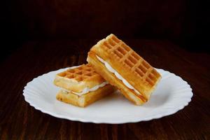 Delicious fresh Viennese waffles with white cream lie on a white plate. photo