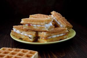 A pile of fresh Viennese waffles lie on and next to a yellow plate. photo