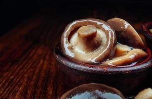 Beautiful delicious pickled mushrooms in a clay cup on a wooden table . photo