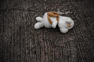 el oso de peluche solitario duerme en el piso de cemento para crear una postal de niños desaparecidos internacionales, corazón roto, solitario, triste, solo, lindo muñeco perdido no deseado. foto