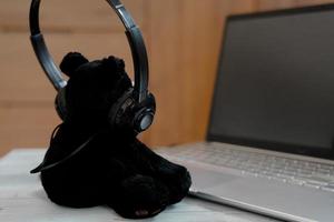 Little bear wearing headphone listen music from laptop, relaxing time. photo