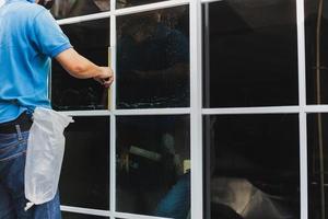 Worker use scraper cleaning window before installing tinting film. photo