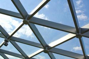 Transparent glass dome roof of modern design style pavilion building with geometric metal construction pattern. View of blue sky and clouds. Abstract structure triangle high-tech architecture window. photo