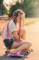 A teenage girl with pink pigtails sat down on a penny board and thought. A girl on a sunny day. photo