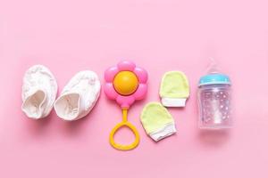 booties, mittens, rattle and bottle on a pink background photo