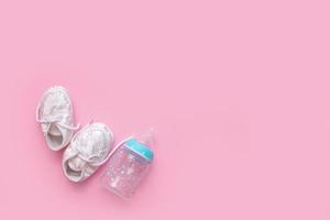 baby booties and a bottle for formula on a pink background with copy space photo